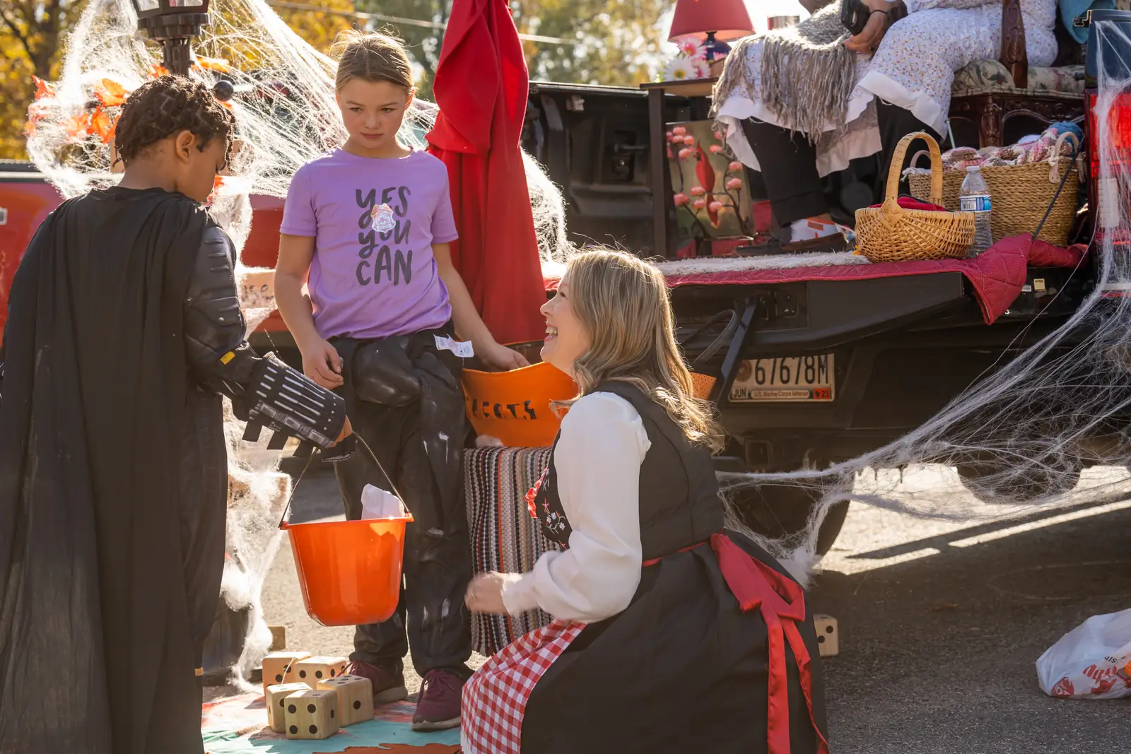 A volunteer in costume handing out candy at a decorated trunk with spiderwebs