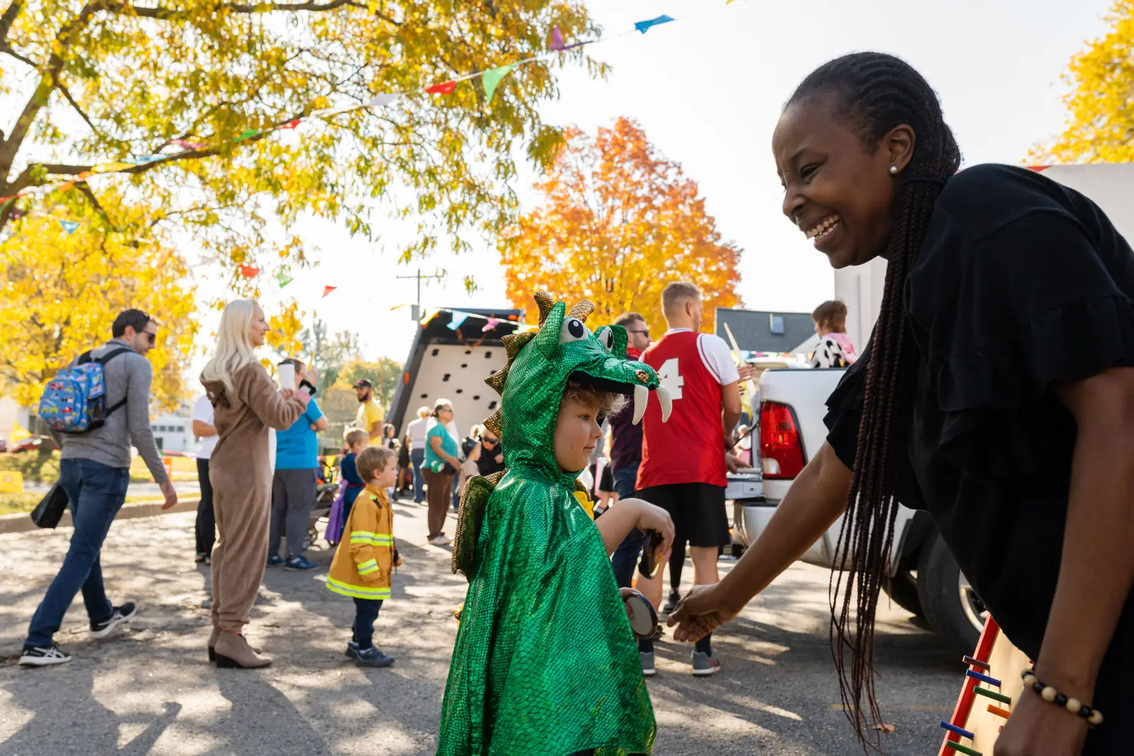 A child in a green dragon costume getting candy from a volunteer