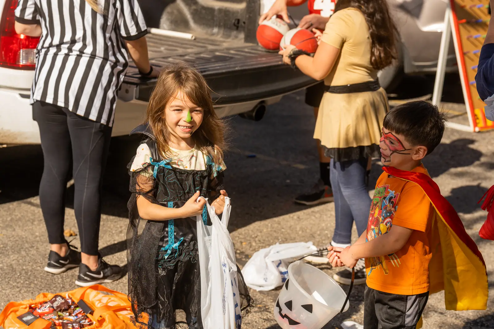 Two kids in costumes smiling with their candy bags at Trunk or Treat